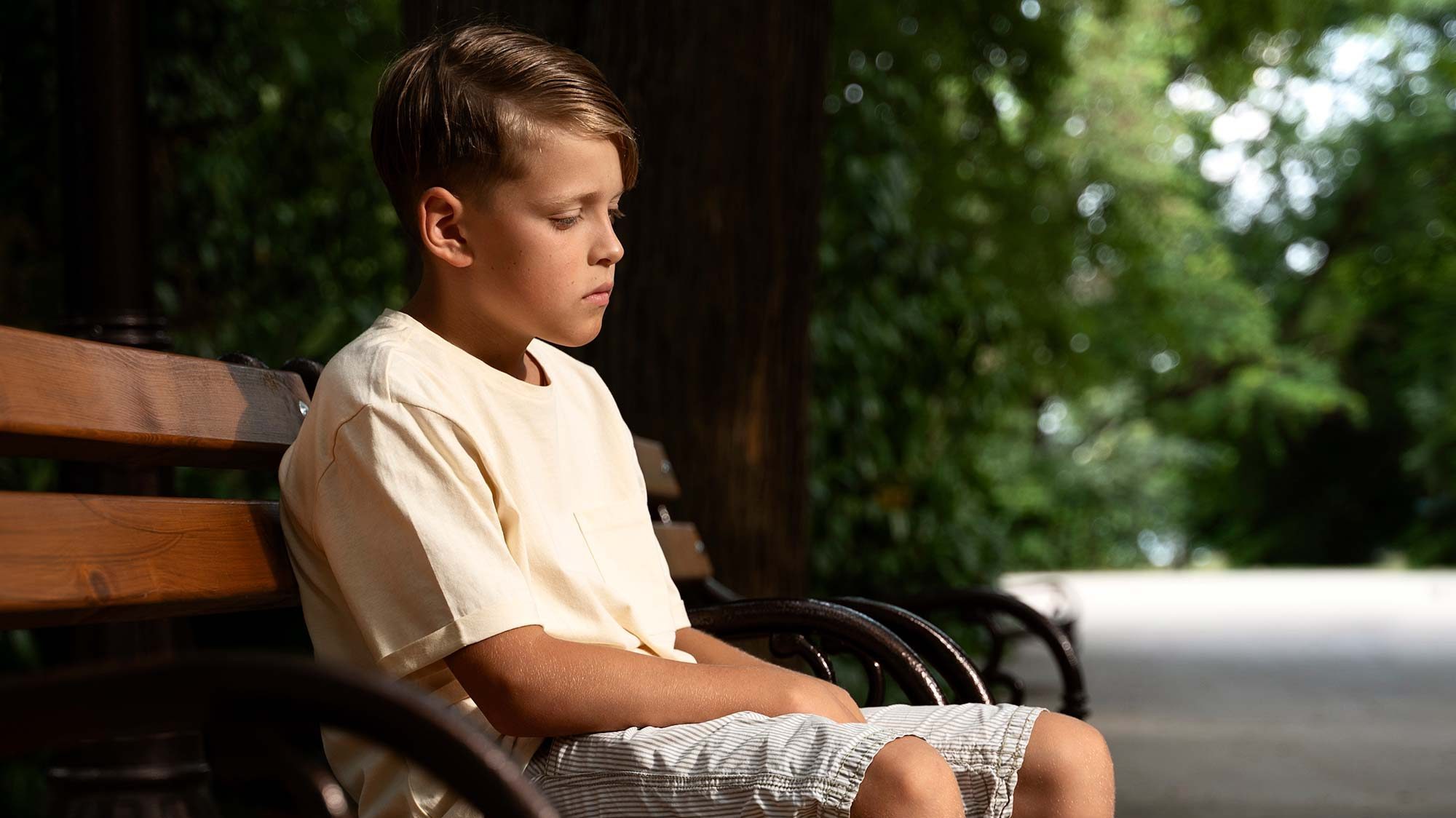 full shot of a sad boy sitting on a bench